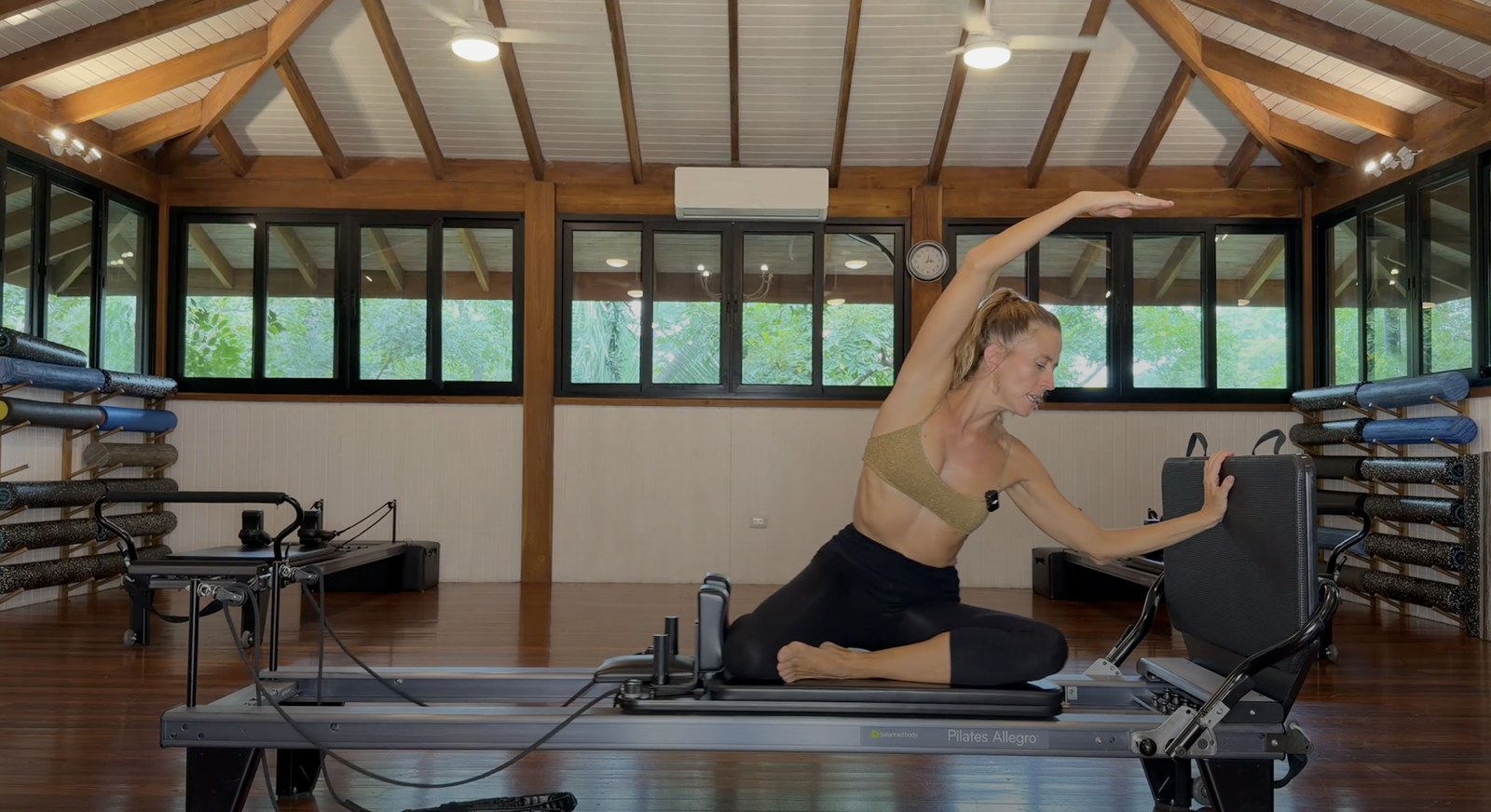 Pilates instructor demonstrating a seated side stretch on a reformer