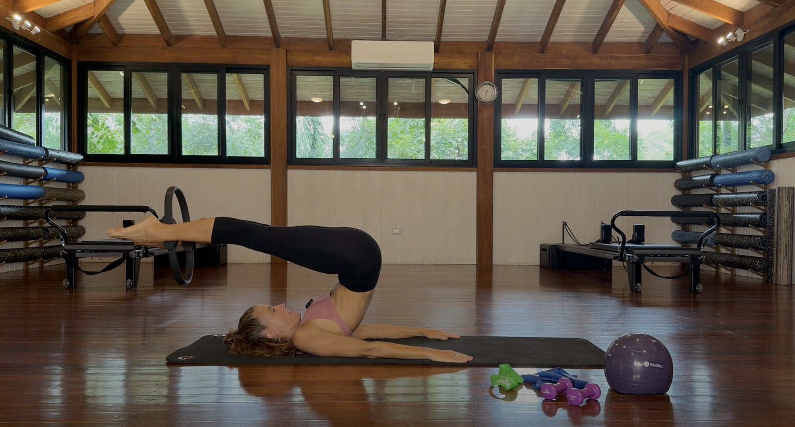 Pilates instructor lifting her legs overhead on a mat with a Pilates ring